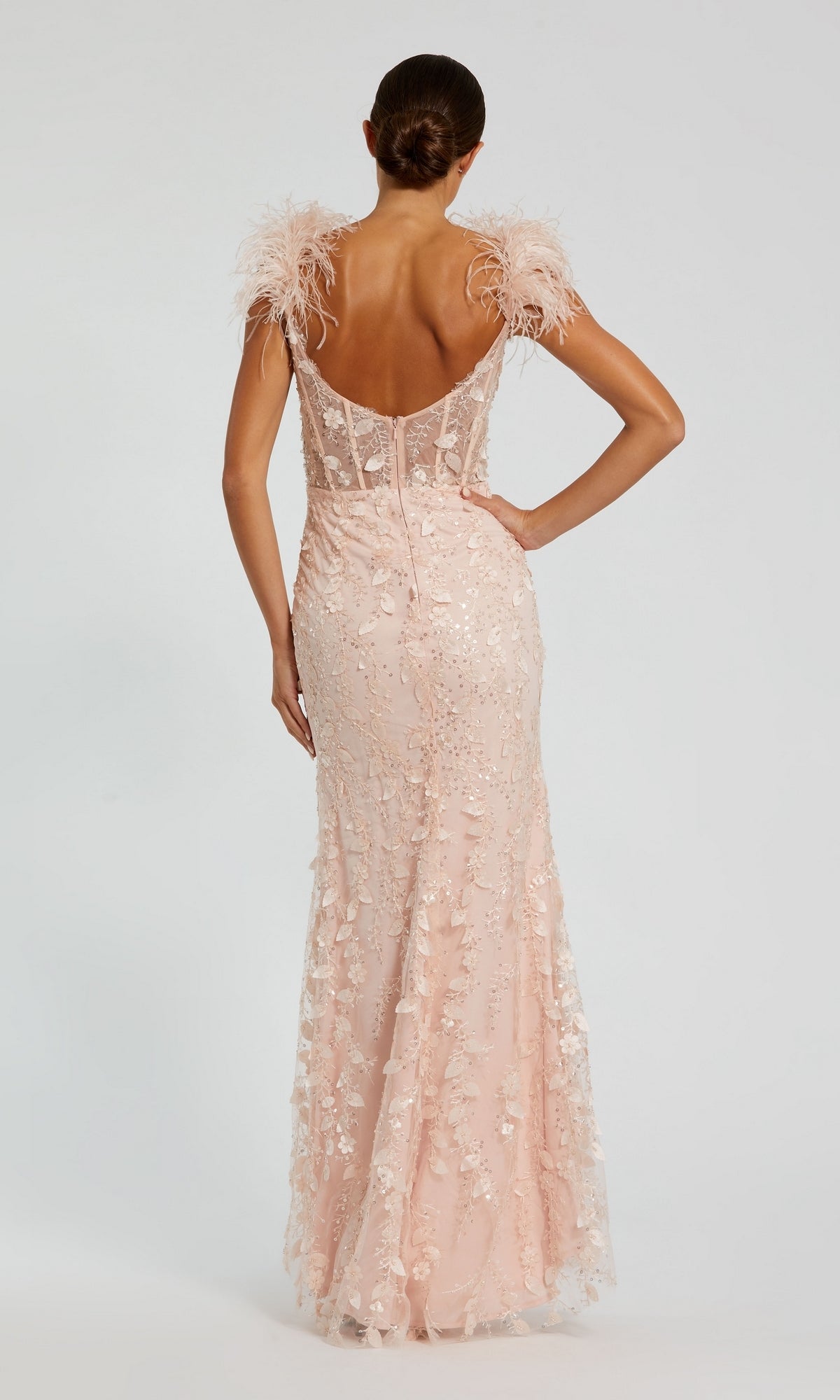 A woman stands with her back to the camera, wearing the Mac Duggal Long Formal Dress 20889—an elegant pale pink, floor-length gown with a sweetheart neckline, feathered shoulders, and delicate floral embellishments.